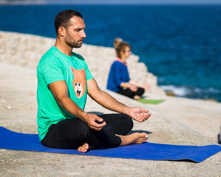 A few people doing a yoga meditation pose on a rocky beach in sunshine right by the sea